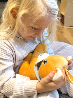 Ein Kind sitzt gemütlich und hält Lenabie Tali, den gelben Puma-Plüschcharakter, liebevoll im Arm. Das Kind blickt lächelnd nach unten auf Tali, die einen altersgerechten Lerninhalt über den eingesetzten Lenabo Smart Speaker wiedergibt. Die Szene wirkt ruhig und warm, in einer warmen Wohnatmosphäre.